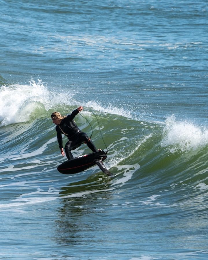 A professional surfer in a sleek wetsuit skillfully rides a powerful wave on his surfboard, displaying exceptional balance and contro